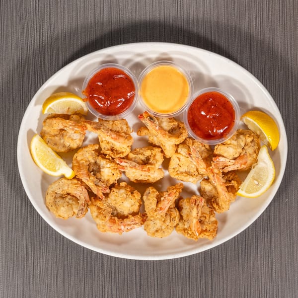 A white oval platter filled with golden fried shrimp, lemon wedges, and three dipping sauces.