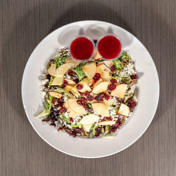 Overhead view of a vibrant salad with apples, cranberries, feta, and two cups of dressing.