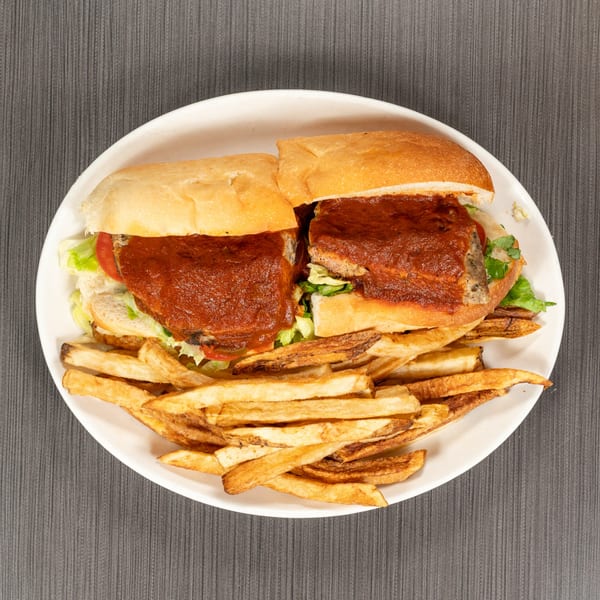 Two halves of a meatball sub with red sauce, lettuce, and tomato, served with fries.