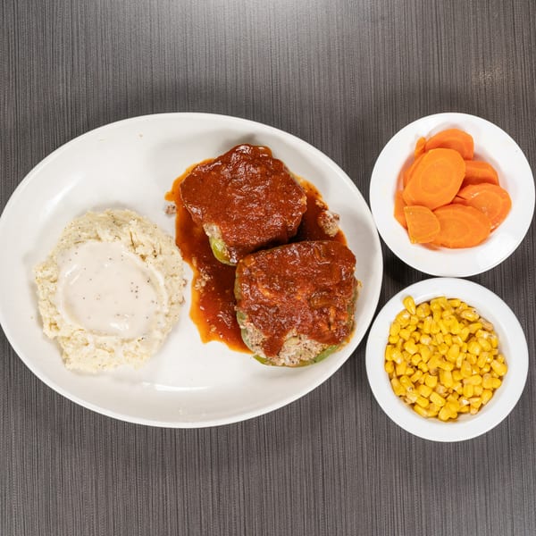 Two stuffed bell peppers with red sauce, mashed potatoes with gravy, carrots, and corn.