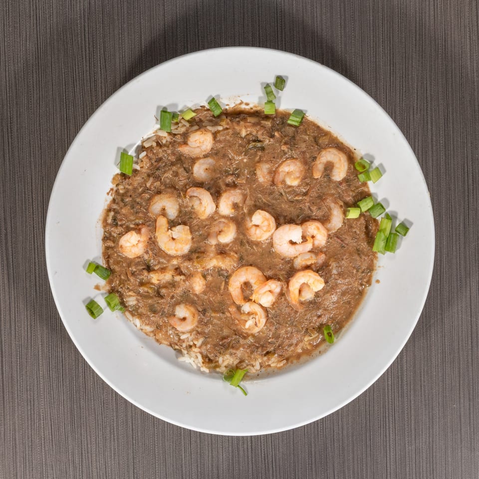 Overhead view of shrimp gumbo with rice and green onions on a white plate.