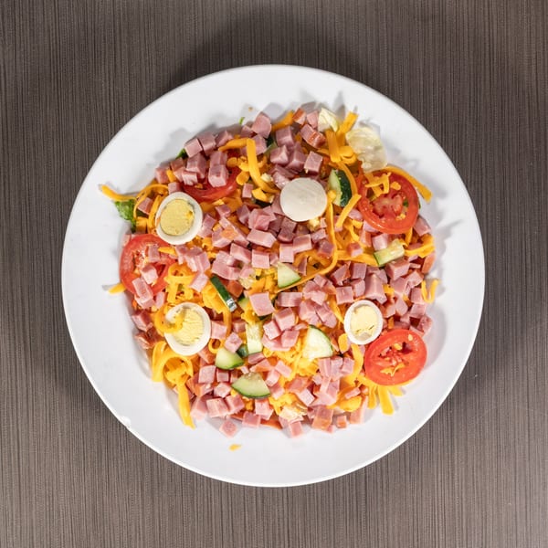 Overhead view of a chef salad with ham, cheese, tomatoes, cucumbers, and hard-boiled eggs.